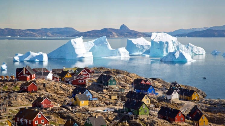 Colorful houses dot a rocky bluff overlooking the ocean, icebergs, and mountains, in the greenland, the arctic circle