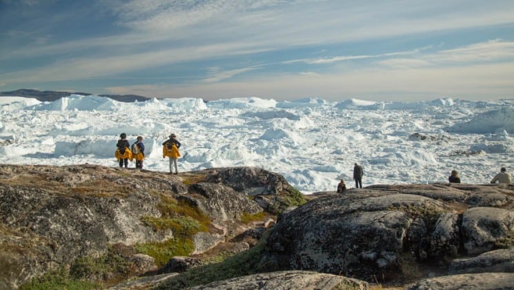 with icebergs in the distance, people hike on an expedition to explore greenland, the southern coasts, and disko bay in the arctic
