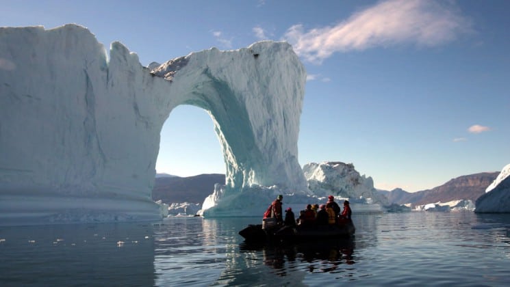 a zodiac boat full of passengers from the scoresby sund adventure cruise get a close look at an iceberg with an arch