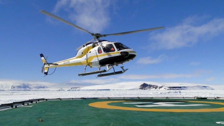 A helicopter lands on a pad surrounded by ice in antarctica, as part of an expedition with weddell sea emperor penguin voyage luxury cruise