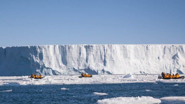 sea kayaks are dwarfed by the size of a glacier and sheer cliff of ice in the arctic