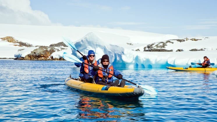 Guests from the National Geographic voyage expedition paddle a kayak near icebergs in antarctica