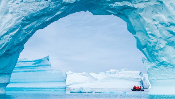 A zodiac motors toward an arch in an iceberg in the ocean in antarctica