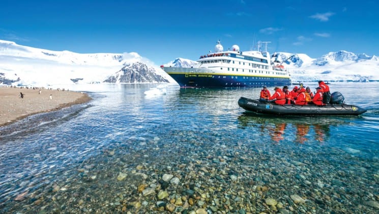 A zodiac boat motors toward the cruise ship that is the national geographic epic antarctica voyage, with icebergs in the background
