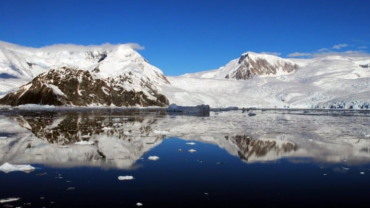 Rocky, snowy mountains are reflected in clear, still water in antarctica's polar circle