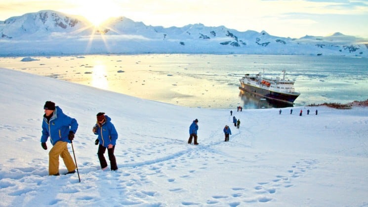 Guests from the national geographic white continent voyage explore neko harbor in the snow while the sun casts golden light over the mountains on the horizon in antarctica