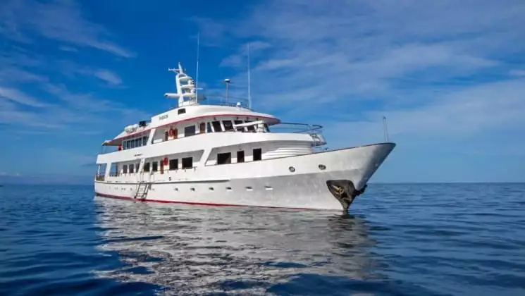 A luxury yacht, the Passion motors over calm, blue waters with the sky and clouds in the background at the Galapagos islands