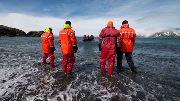 Four people on the expedition team launch a zodiac into the ocean in antarctica