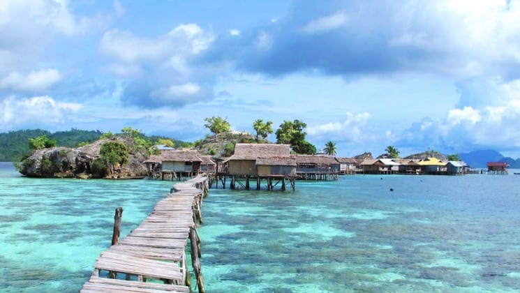 Looking toward an island in indonesia from the end of a long wooden pier over clear, tropical water