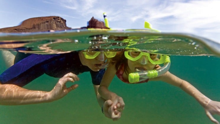 Two children with snorkels and face masks swim in the water near the National Geographic Endeavor, a luxury cruise vessel for traveling to the Galapagos Islands.