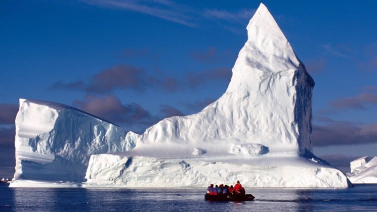 A zodiac full of passengers from the weddell sea emperor penguin voyage cruise motors up to an iceberg in antarctica