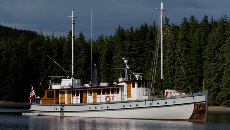 westward alaska small ship anchored on still water with forest behind it