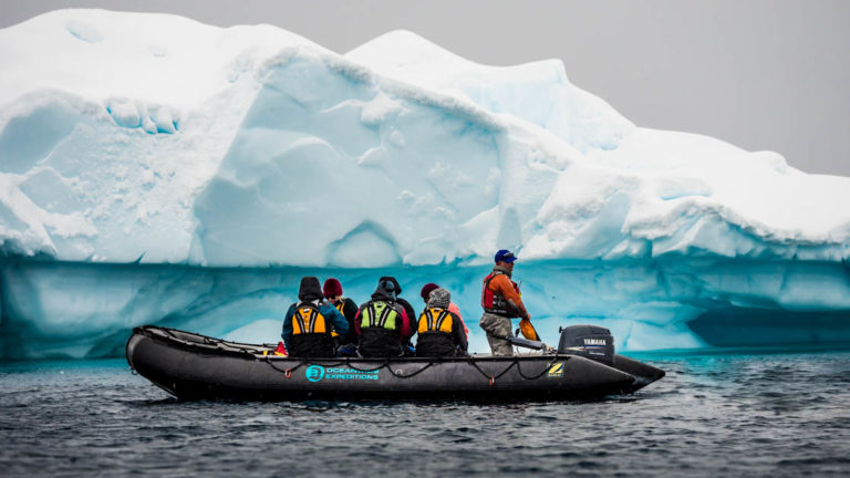 group of travelers in a zodiac skiff looking at a turquoise antarctica icebergy