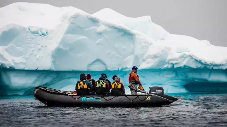 group of travelers in a zodiac skiff looking at a turquoise antarctica icebergy
