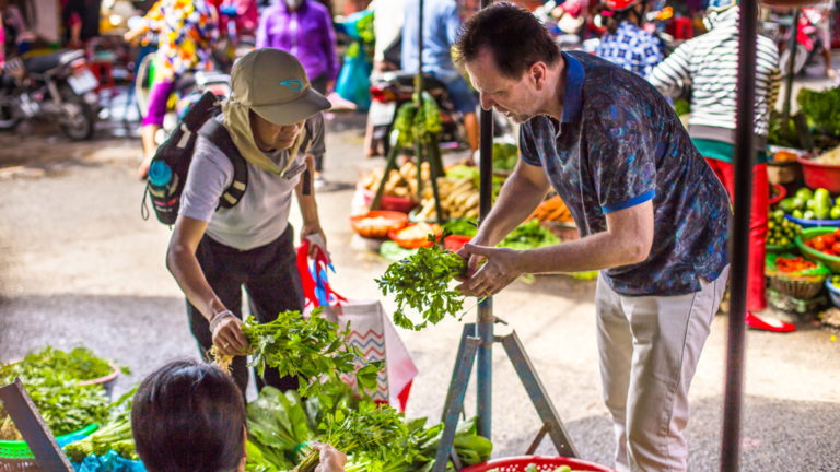 Travelers with chef David Thompson shopping for fruits and vegetables at the local outdoor market.