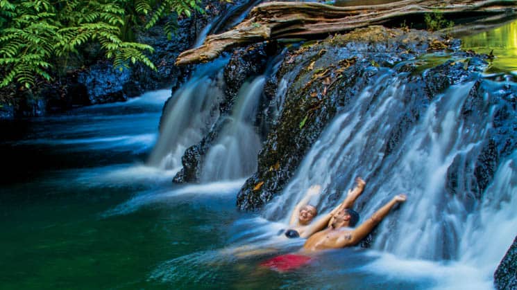 two travelers relax against a rock while water flows over it in the jungle of Corcovado National Park, Costa Rica