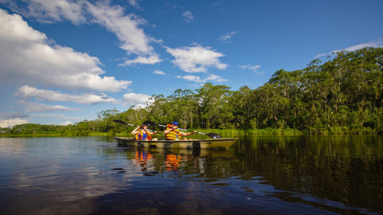 group of adventure travelers in a small motorized boat cruising down the amazon on a calm sunny day with the jungle in the background
