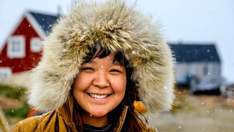 local greenlandic inuit woman smiling with a fur hat and snow falling