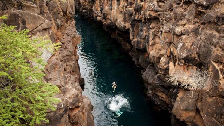 solo traveler on the galapagos discovery land tour in mid air between 2 cliffs above a narrow strip of water