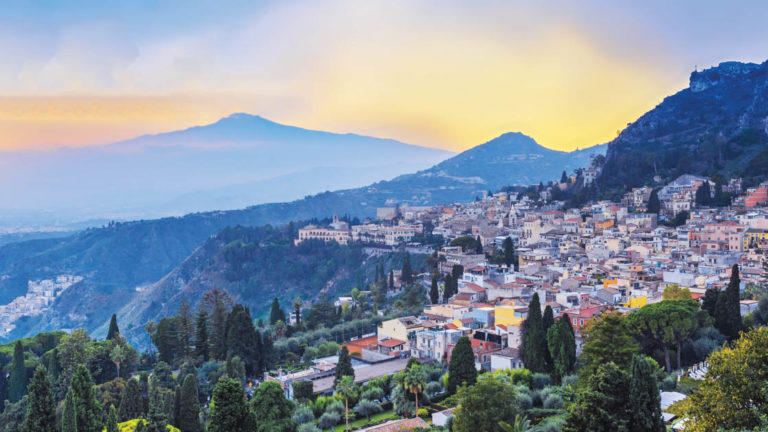 The italian village of taormina on the hills of sicily with many trees at sunset