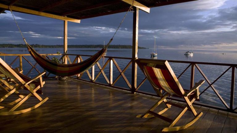A hammock and rocking chairs on the deck of Bocas Del Toro lodge in Panama as the sun sets.