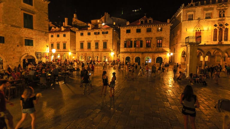 Historic Old Town of Dubrovnik, Croatia at night. Glowing street lights light up a busy street square seen on the under sail small ship cruise from Greece to the Dalmatian coast