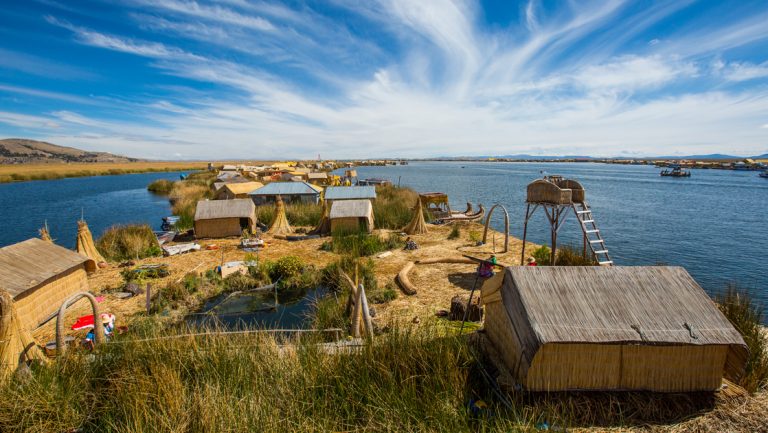 looking down a strip of dry land with hugs and various structures on it with the water of lake titicaca peru on either side