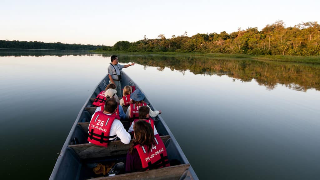 Guide standing at the front of a canoe pointing out sites and sharing his knowledge to the group on an excursion in the amazon