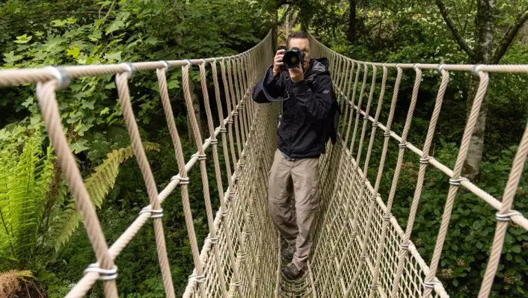 Photographer takes photo on rope bridge in lush gardens of Cornwall, England during the Ancient Isles Nat Geo cruise.