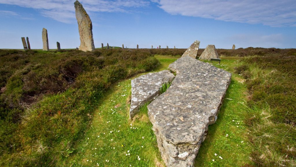 Ring of Brodgar ancient stone circle sits in green grass under blue skies in Orkney Islands, Scotland.