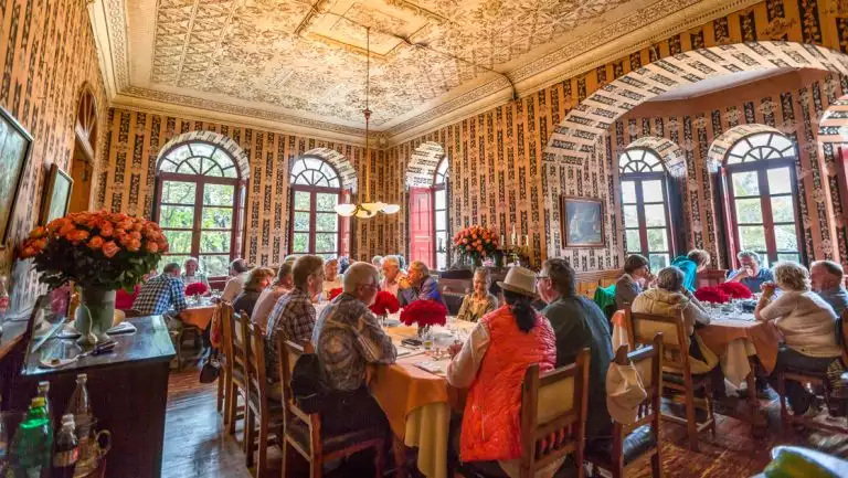 Ecuador's Andes Highland Haciendas travelers sit at a luncheon at a rose plantation in an ornate room with high ceilings.