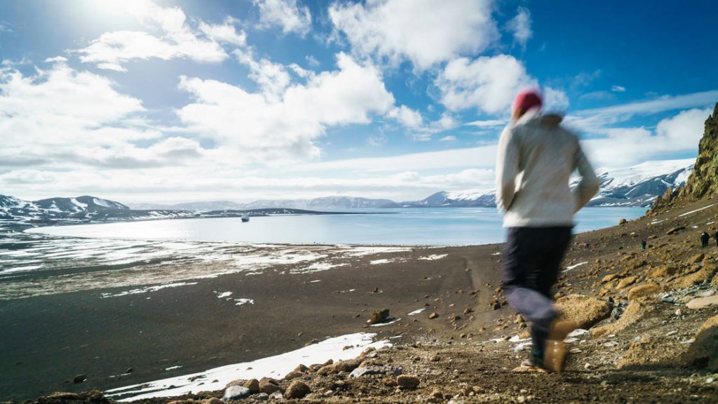 Hiker walking along the Antarctica Peninsula in the South Shetlands islands with sun and clouds.