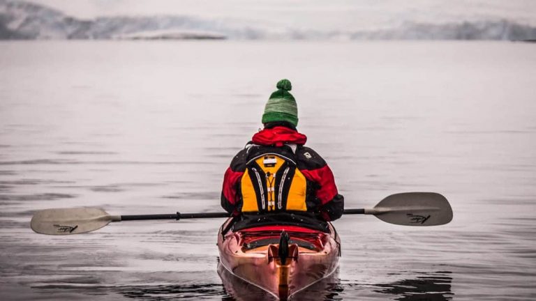 Guest kayaking with beanie with the Antarctic Peninsula in the backgorund