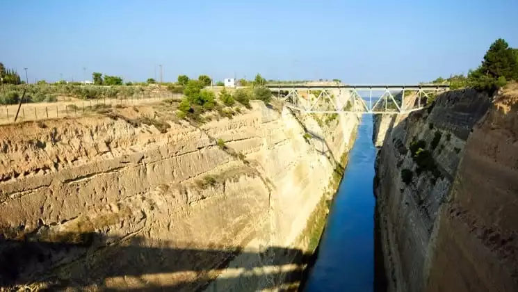 a canal runs between dirt slopes in corinth, leading to the aegean sea