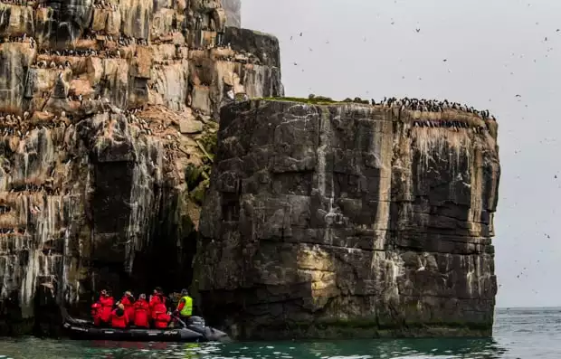 A group of travelers on a skiff in the Arctic waters, in front of a rocky cliffside