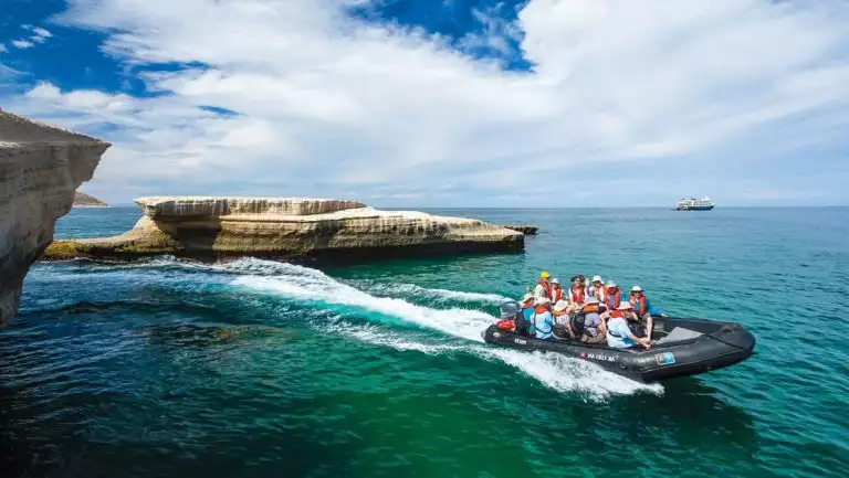 Zodiac with Baja travelers zooms through emerald waters on a sunny day during the Remarkable Journey cruise.