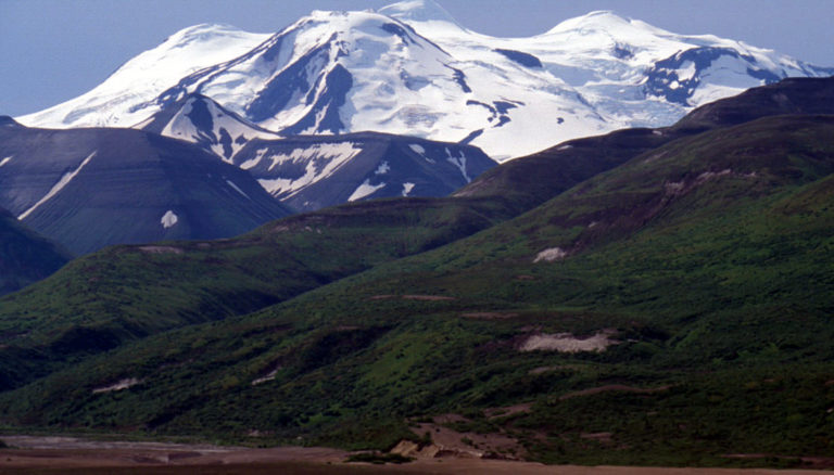 green hilly mountains in front of larger snow capped peaks in the katmai peninsula of alaska