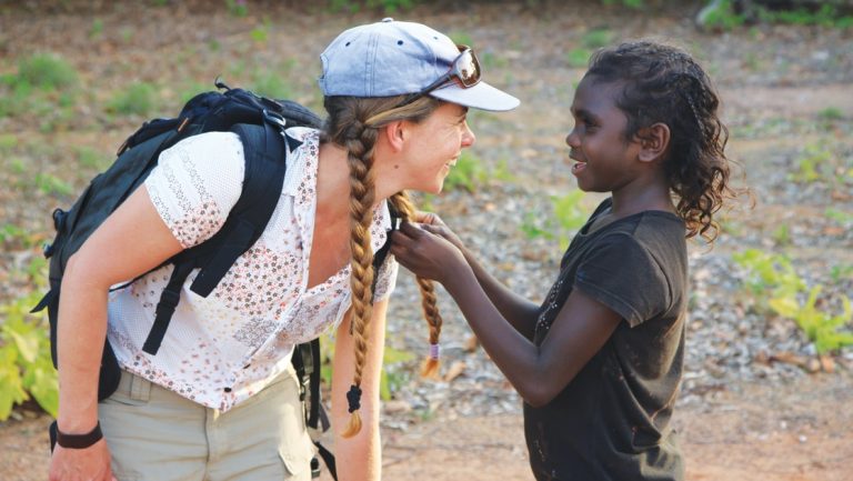 Woman traveler leans down to talk with a boy during a Cape York & Arnhem Land small ship cruise in northern Australia.