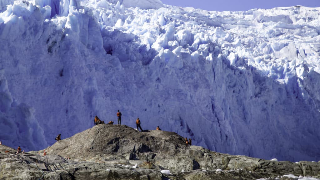 Several people standing on rocks in front of a massive blue and white glacier in Patagonia