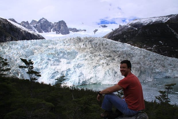 A traveler smiling while sitting and looking at a tidewater glacier in Patagonia.
