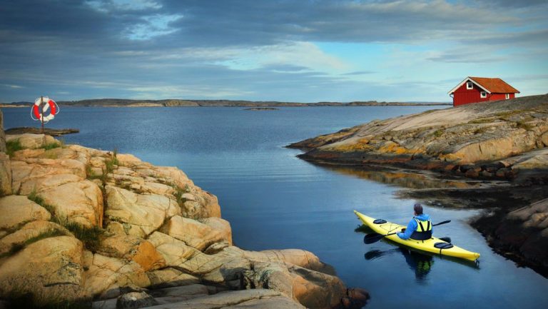 Solo kayaker in yellow boat sits in inlet between smooth rock shoreline during the Circumnavigating the Baltic Sea Cruise.