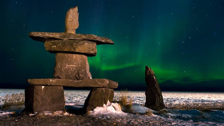 A rock statue in Churchill, Canada with green northern lights shining.