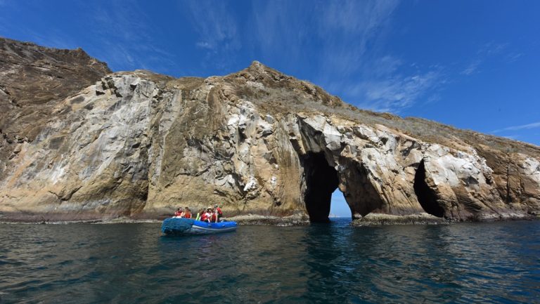 An inflatable zodiac boat filled with travelers in life jackets navigates the waters and rock formations around San Cristóbal Island