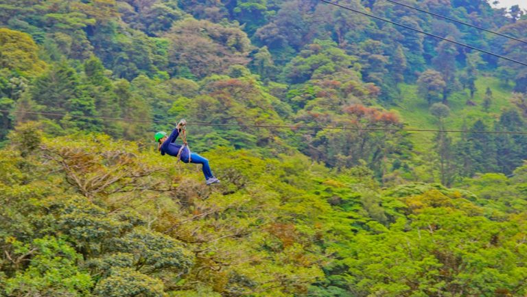 Girl zip lines above bright green rainforest on a sunny day during the Costa Rica Family Adventure.