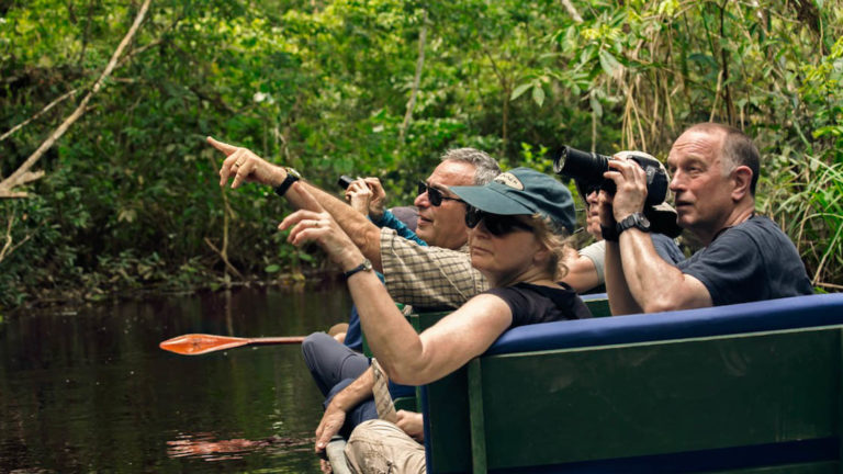 amazon travelers in a small boat look and point into the jungle at the napo wildlife center