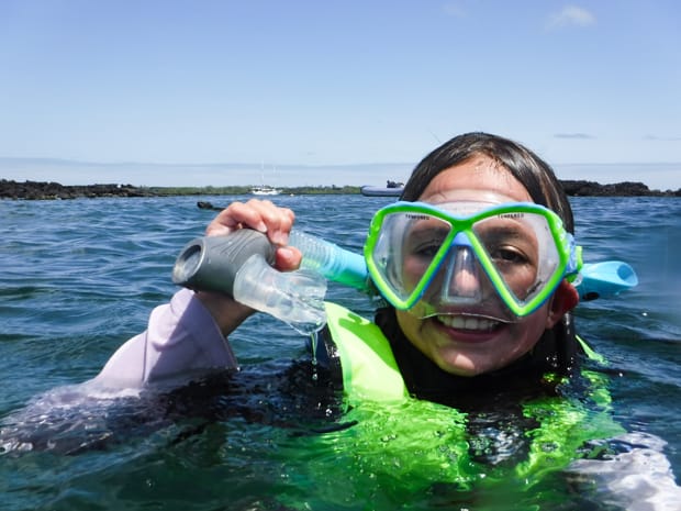 During a Galapagos cruise activity, A young girl snorkeling in the Galapagos on a blue sky day wearing lime green life jacket and mask.
