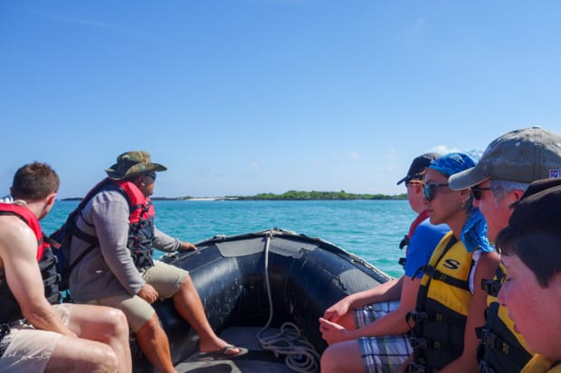 As part of a Galapagos cruise activity, A group of Galapagos travelers ride on an inflatable skiff with a guide, infront of them the blue cloudless sky drop to the teal water horizon.