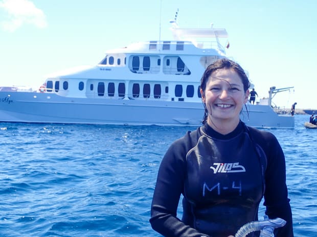 A woman in a wetsuit in front of a Galapagos small ship smiling after snorkeling on a Galapagos small ship cruise 