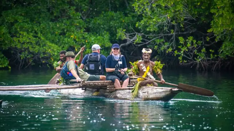 Frontier Lands of New Guinea cruise guests ride in a wooden carved canoe paddled by native locals in celebratory dress.