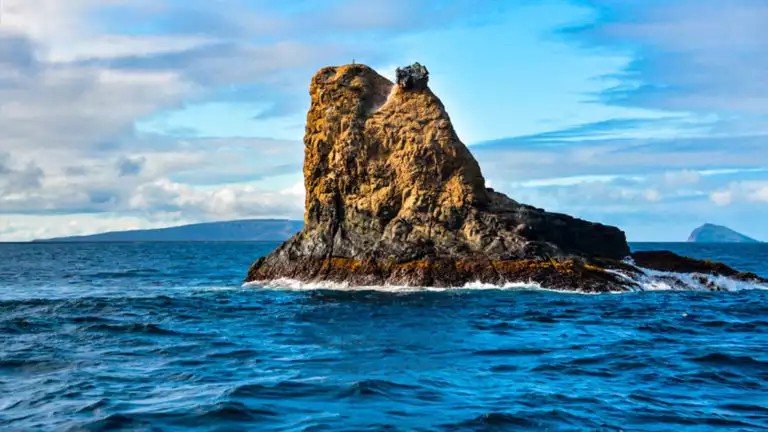 Pinnacle Rock juts above the ocean under the sky with clouds at the Galapagos Islands